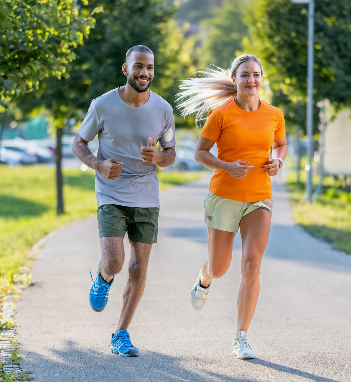 A man and a woman jogging side by side along a scenic pathway lined with trees.
