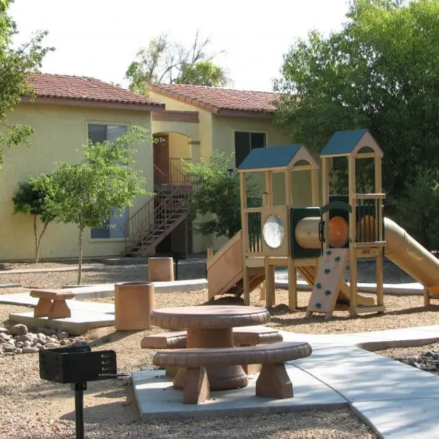 Outdoor Playground Area A playground with a slide and climbing structure in an outdoor area, surrounded by trees and benches, with buildings in the background.
