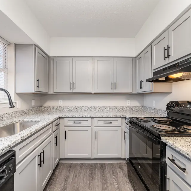 A modern kitchen with gray cabinets, granite countertops, and a black stove.