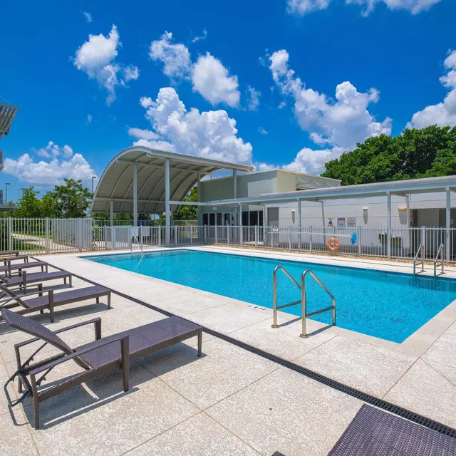 Fenced in swimming pool surrounded with lounge chairs and a white gate.