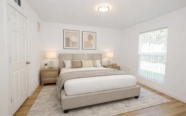 Modern Minimalist Bedroom Interior A minimalist bedroom featuring a queen-size bed with soft linens, two bedside tables with lamps, and abstract art on the walls. There's a large window allowing natural light and a light wooden floor.