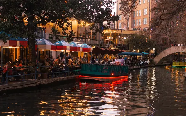 Riverwalk area at night behind 120 Ninth Street apartments, featuring a ferry boat in water with patrons floating next to restaurant outdoor dining.