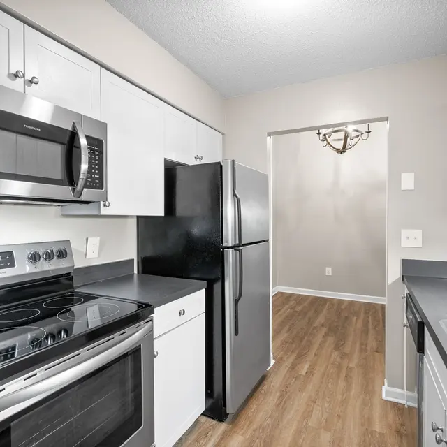 A modern kitchen featuring stainless steel appliances, light gray cabinets, and wooden flooring. The space includes an oven, microwave, and refrigerator.