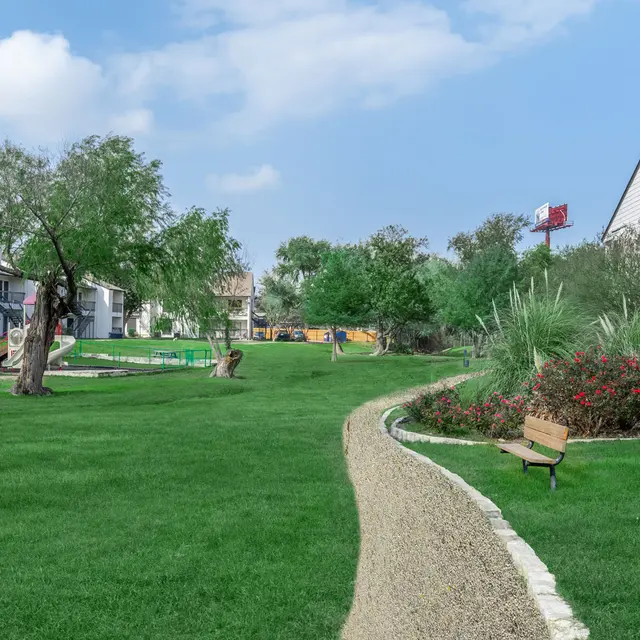 Lawn and walkway at Aviva at North Plaza surrounded by trees, gardens, and apartment buildings.