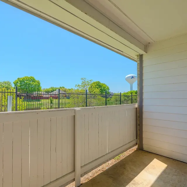 A balcony area with a white wooden railing overlooking a green landscape on a sunny day.