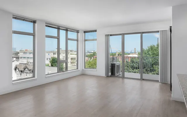 Bright, empty room with large windows and balcony offering a city view.