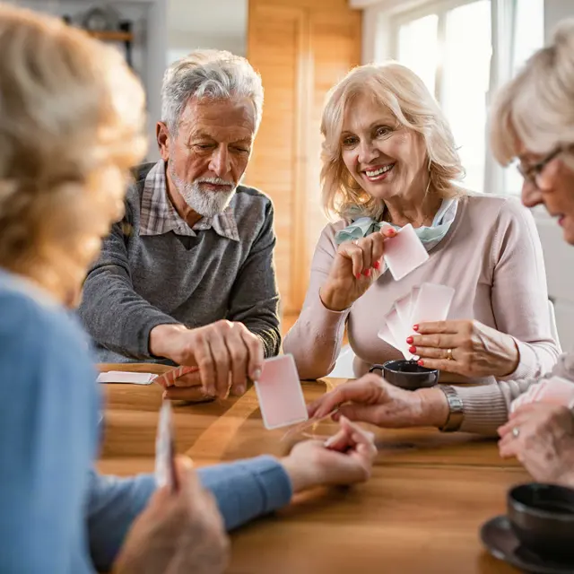 A group of elderly people sitting around a table, engaging in a card game. They are smiling and interacting with each other, with cups of coffee in front of them.