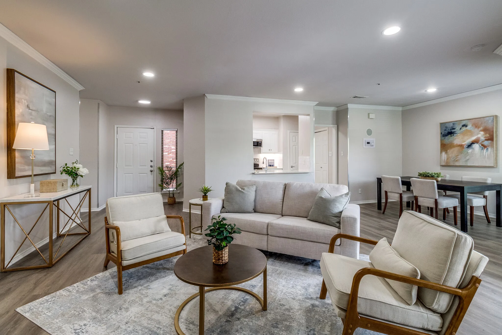 Modern Living Room Design A modern living room featuring a light gray sofa, two cream-colored chairs, a round coffee table, and a decorative area rug. The space is bright and airy with a doorway leading to a kitchen area and dining space visible in the background.