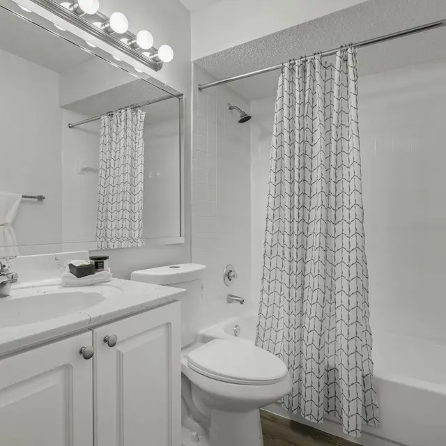 A modern bathroom featuring a clean white design, with a bathtub, shower, mirror, and sink area.
