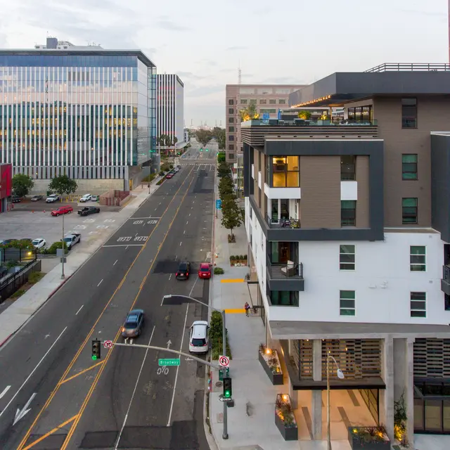 Aerial view of an urban street featuring modern buildings on either side, with a wide road and parked cars.