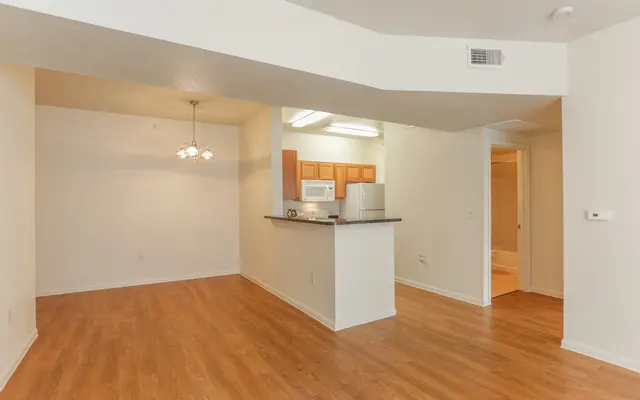Interior view of a modern apartment featuring hardwood flooring, a small kitchen area with a countertop, a dining area with a chandelier, and a doorway leading to other rooms.