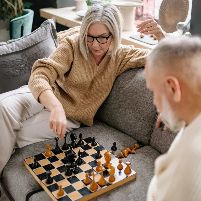 Two people playing chess on a sofa in a cozy living room setting.