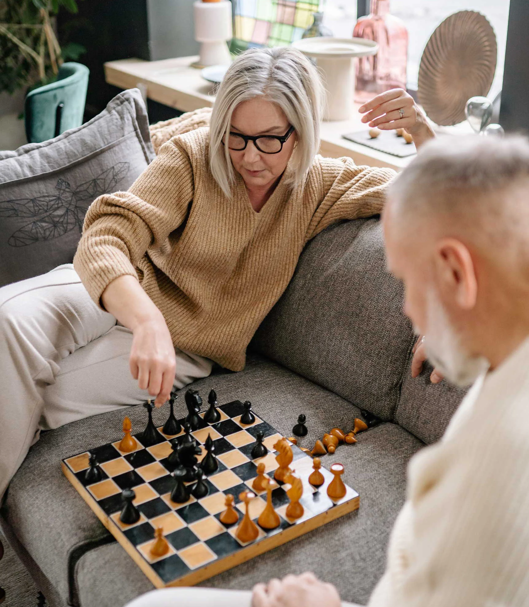 Two people playing chess on a sofa in a cozy living room setting.