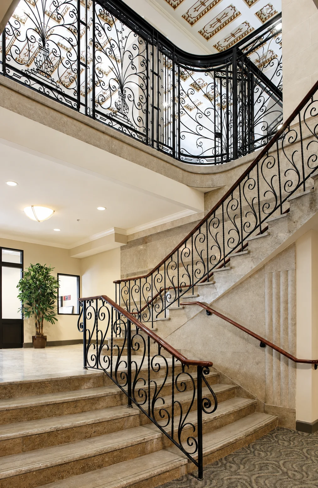 Elegant staircase with ornate railing and decorative ceiling in a well-lit interior.
