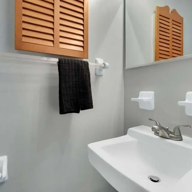 A modern bathroom featuring a white sink, a wall-mounted mirror, and a towel hanging on a rack. The walls are painted grey, and there are wooden slatted shutters above the sink.