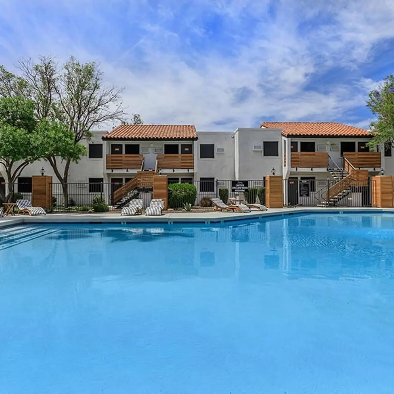 A tranquil swimming pool surrounded by landscaped greenery and a multi-story residential complex with balconies.