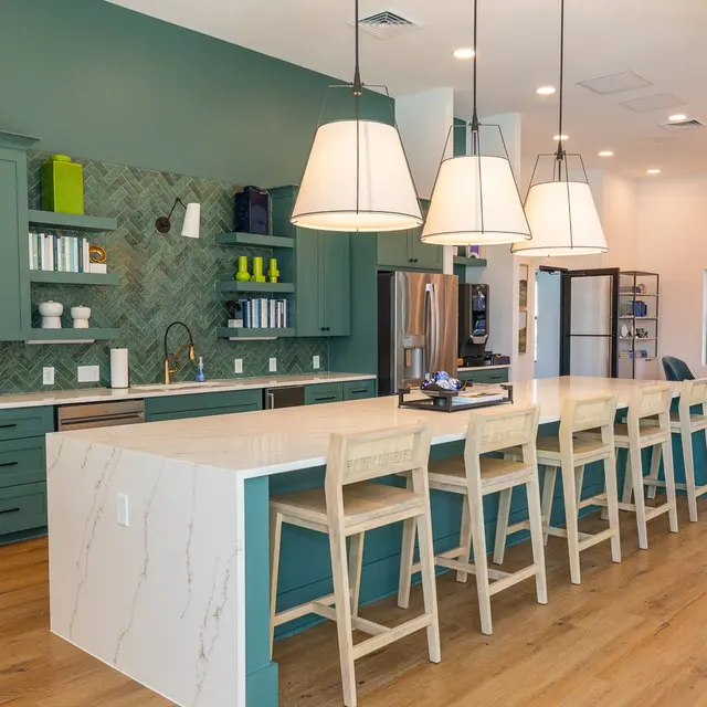 A modern kitchen featuring teal cabinetry, a large marble island with bar stools, and contemporary pendant lighting. A geometric tile backsplash enhances the design. 