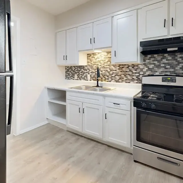 A modern kitchen featuring sleek white cabinets, a black stove, and a stainless steel refrigerator.