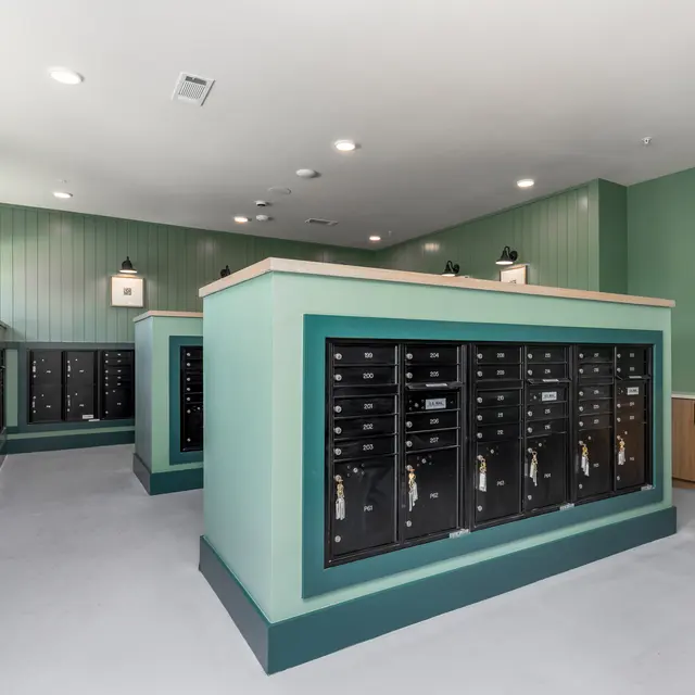 A modern mailroom featuring multiple black mailboxes arranged in elegant structures with a green and natural wood color scheme.