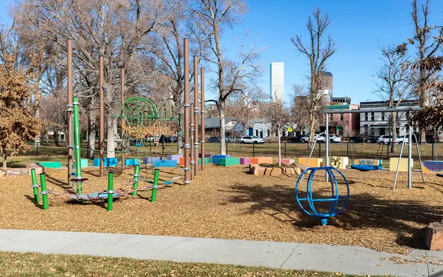 BOUNDLESS CREATIVITY A spacious playground featuring diverse play structures, including climbing equipment, swings, and spinning rides, surrounded by bare trees and a clear blue sky.