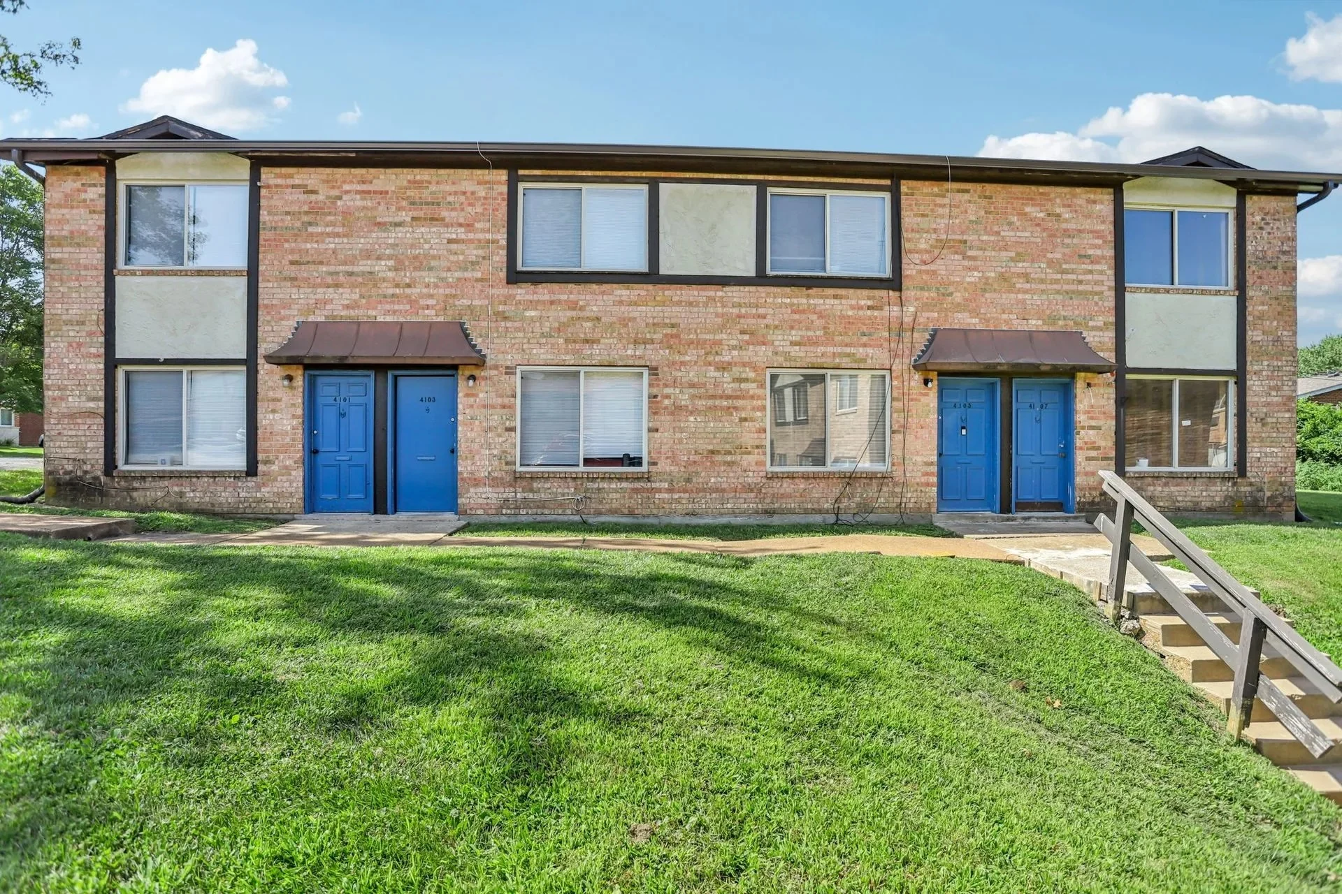 Two-Story Apartment Building Front View Exterior view of a two-story brick apartment building with blue doors and green grass in front.