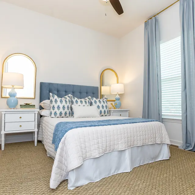 Stylish Modern Bedroom A modern bedroom featuring a blue upholstered headboard, white bedding, and decorative pillows. Nightstands with lamps are on either side, and there are light blue curtains by the window.