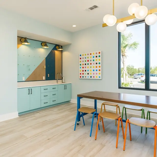 A bright and colorful room featuring a modern table with chairs, large windows, and colorful wall art.
