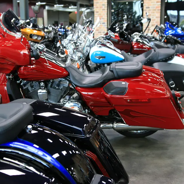 Harley-Davidson Museum A row of motorcycles displayed in a showroom, featuring various colors and styles, including red, blue, and black. The space has a modern design with exposed brick walls and a polished floor.