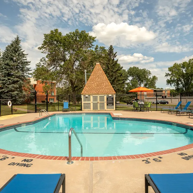 Regency Park - A clean outdoor swimming pool surrounded by lounge chairs and trees under a blue sky with fluffy clouds.