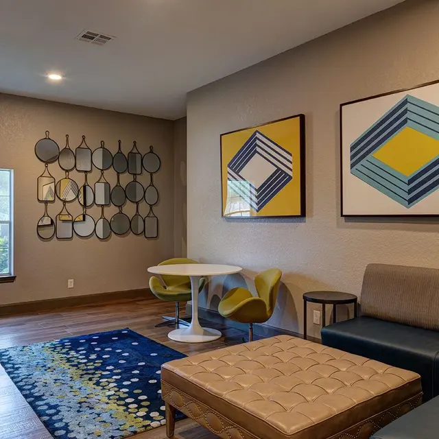 A modern living room featuring a blue and yellow rug, geometric wall art, a sectional sofa, and a circular dining table with yellow chairs.