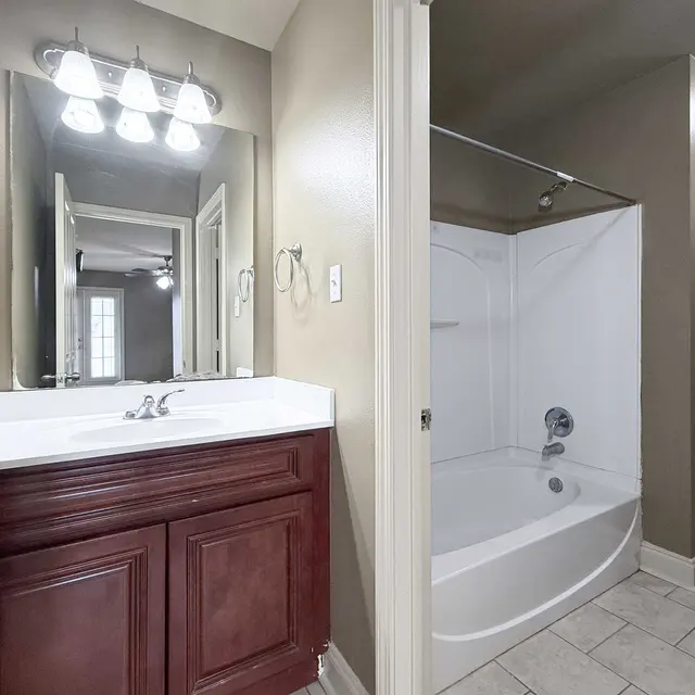 Interior of a modern bathroom featuring a white vanity with a sink and dark wood cabinets, a bathtub with a shower, and light-colored walls.