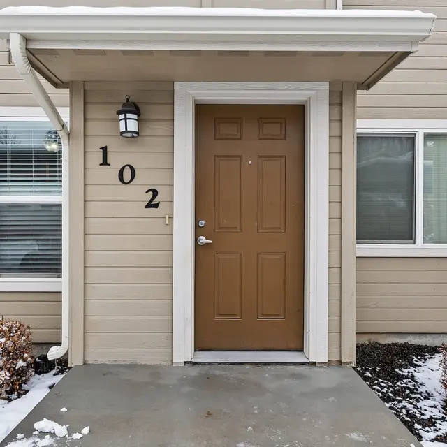 Bowery Point Front view of an apartment entrance with a brown door, number 102, and snow on the ground.