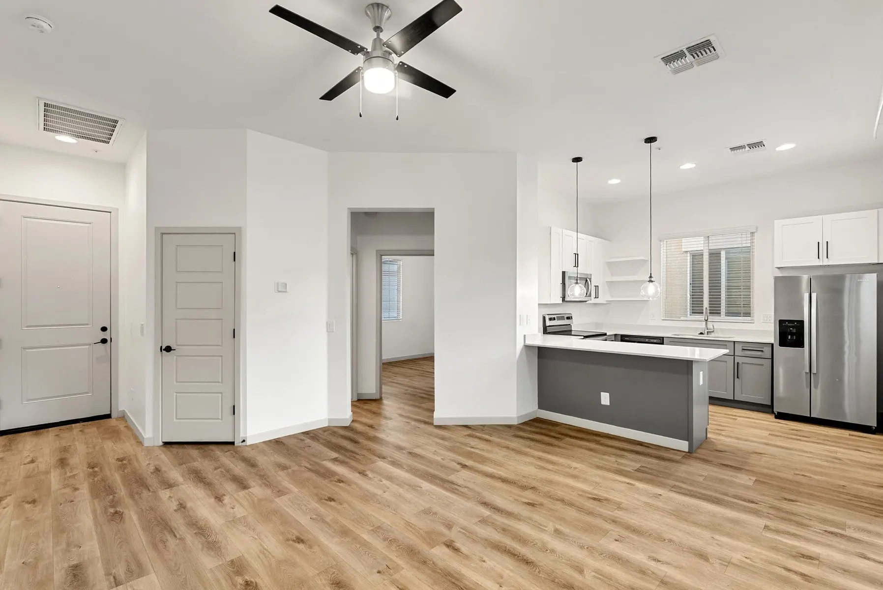 Modern open-concept living space with a kitchen, stainless steel appliances, wooden flooring, and bright natural light.