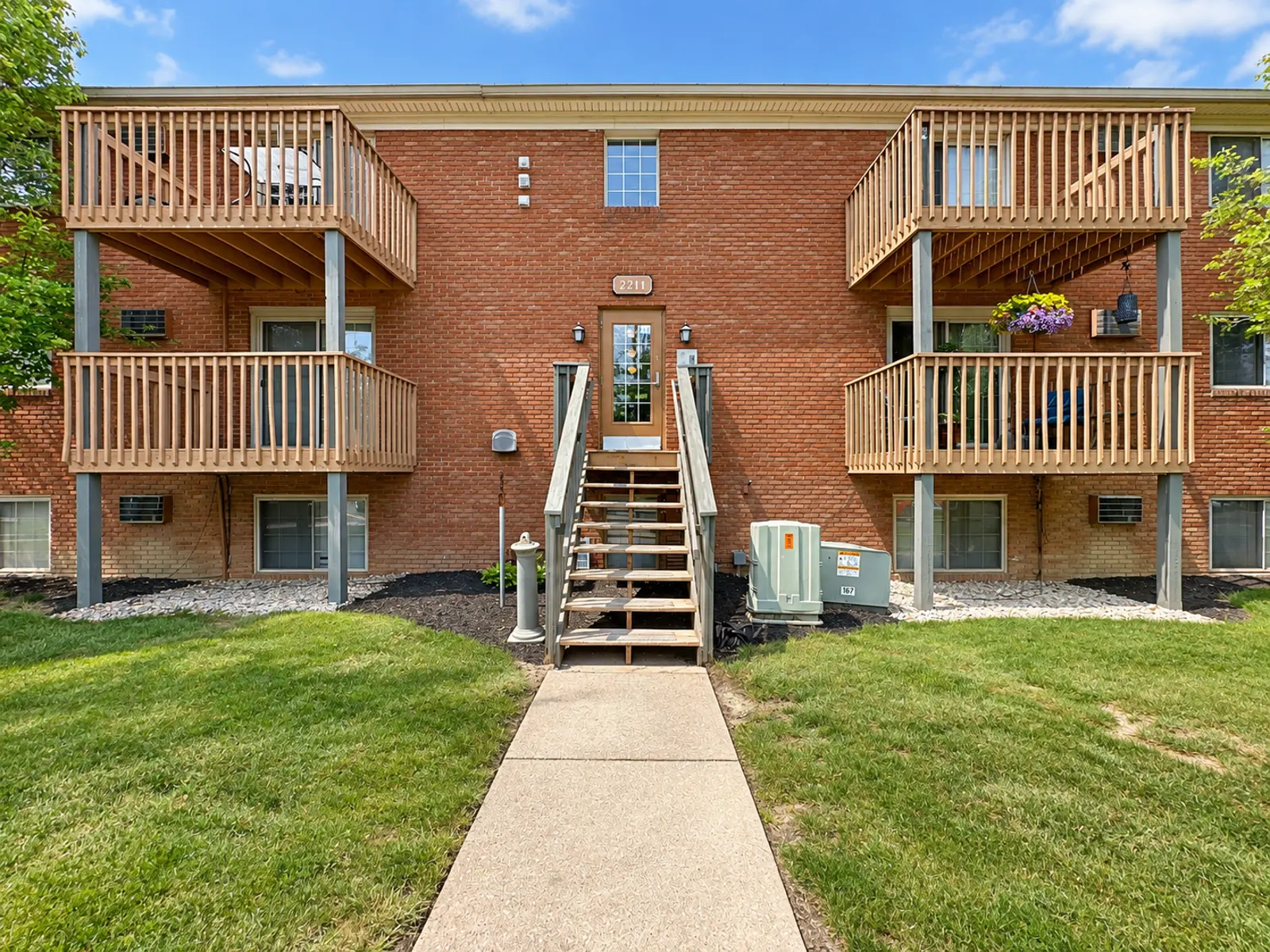 Exterior view of a brick apartment building with two balconies and a central staircase.