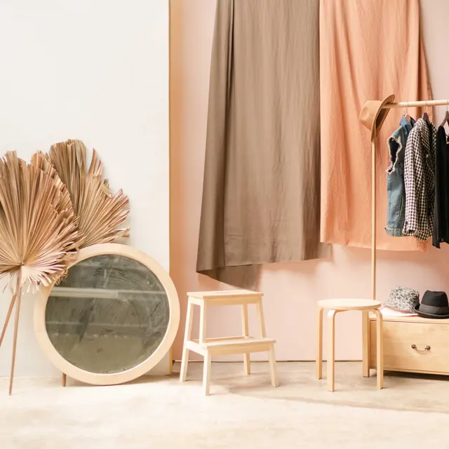 A stylish room featuring minimalist decor, including a mirror, clothing rack, and textured fabric drapes in soft colors.