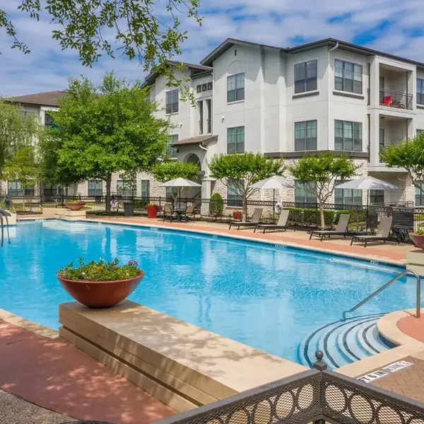 Resident pool with chairs and tables and lounge chairs around the pool, apartment homes in the background in Houston, TX