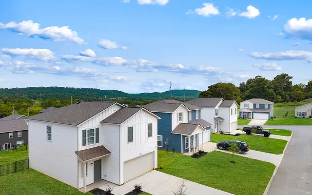 Aerial view of a residential neighborhood featuring modern homes, neatly manicured lawns, and mountains in the background under a blue sky with scattered clouds.
