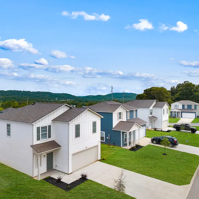 Aerial view of a residential neighborhood featuring modern homes, neatly manicured lawns, and mountains in the background under a blue sky with scattered clouds.