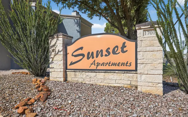 Sign for Sunset Apartments with stone structure and ornamental plants.