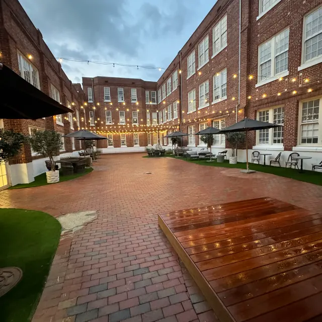 A beautifully designed courtyard surrounded by brick buildings, featuring string lights, paver stones, and areas of green grass.