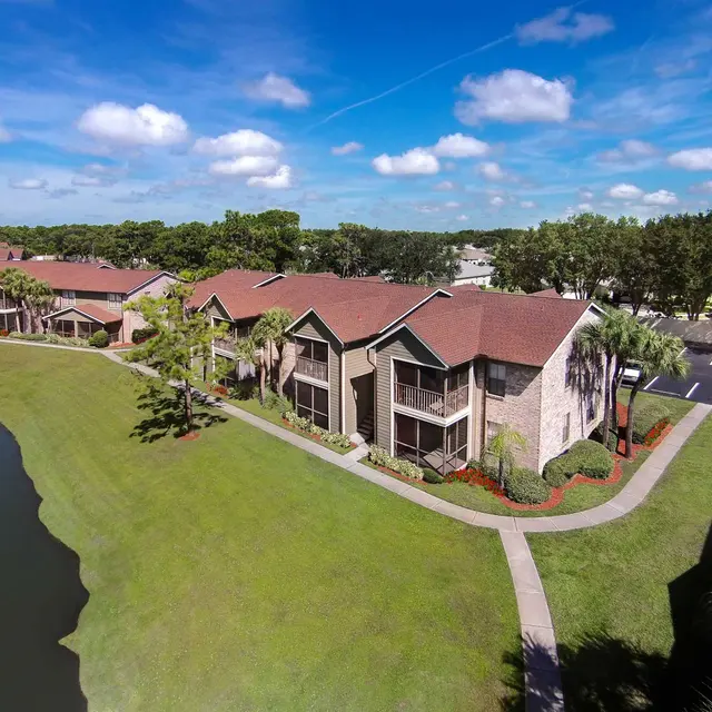 Aerial view of Venice Park Apartments with a sidewalk and grass next to a pond.