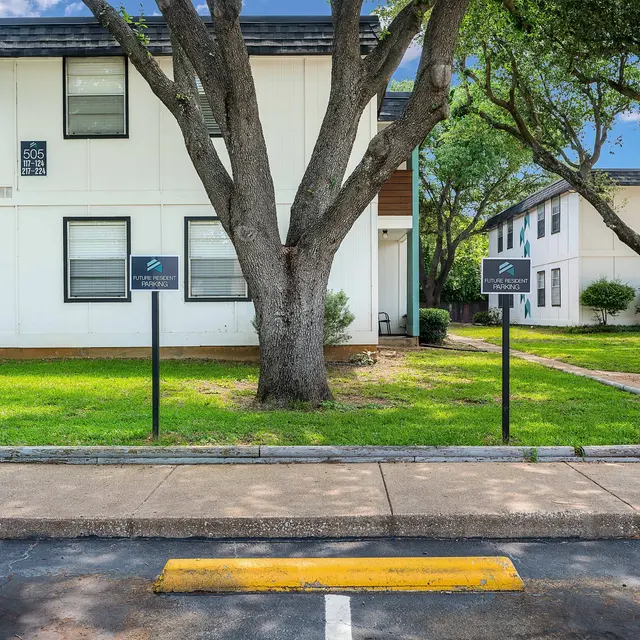 View of a residential apartment complex with two buildings, lush green grass, and trees around.