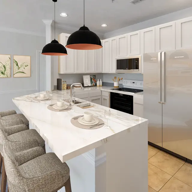 A modern kitchen with a large island featuring four bar stools. The island has tableware set for dining. Above the island, two black pendant lights hang down. The kitchen includes white cabinets, a stainless steel refrigerator, and black stovetop.