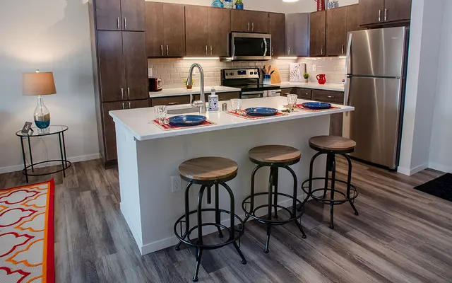 Modern kitchen interior with bar stools, stainless steel appliances, and a neatly set breakfast bar.