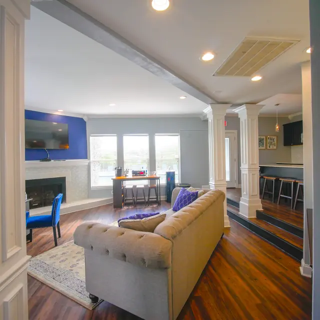 A stylish modern living room with a couch, blue accent wall, and a fireplace, featuring a bright window view and a bar area in the background.