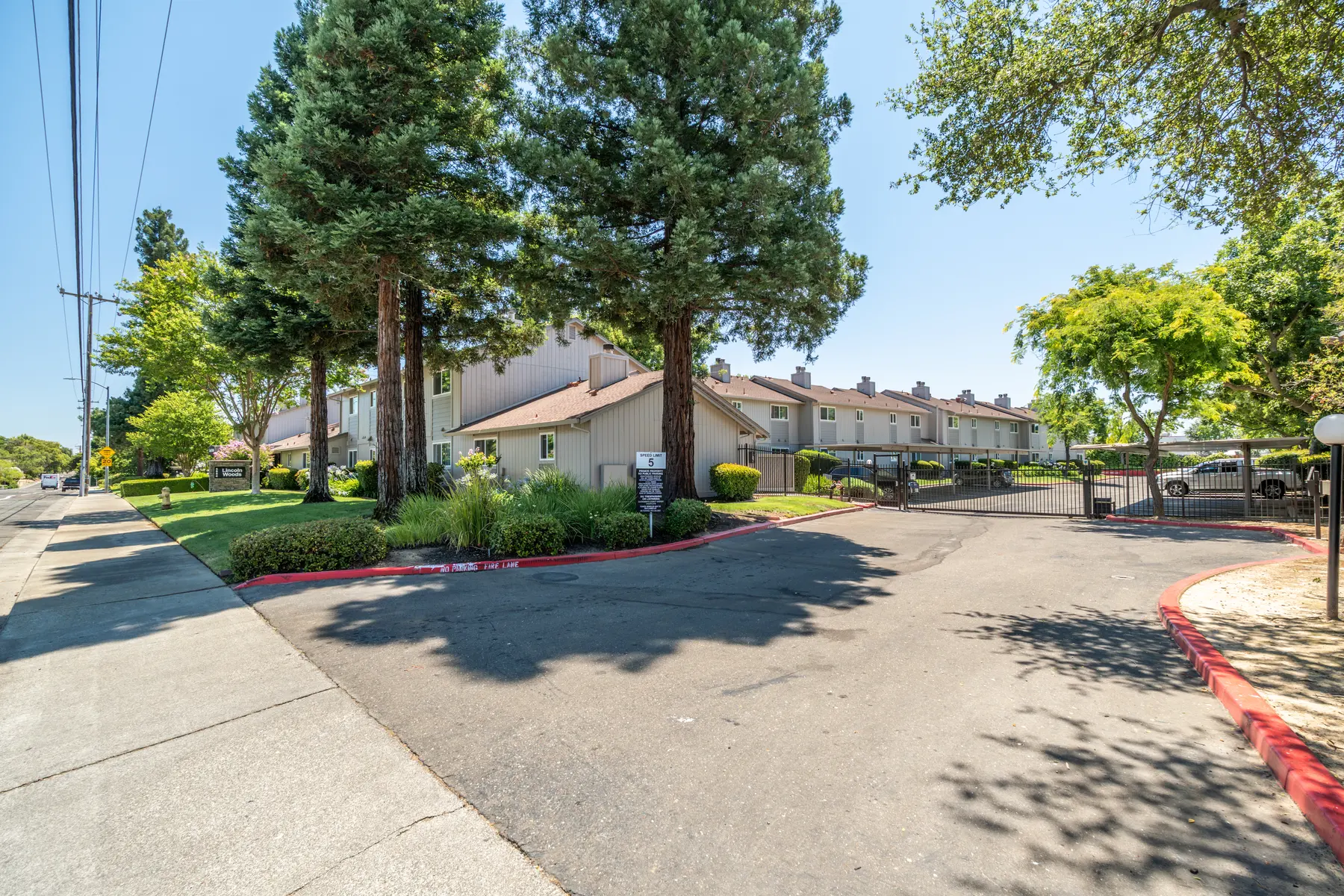 Entrance to an apartment complex featuring several trees and well-maintained landscaping.