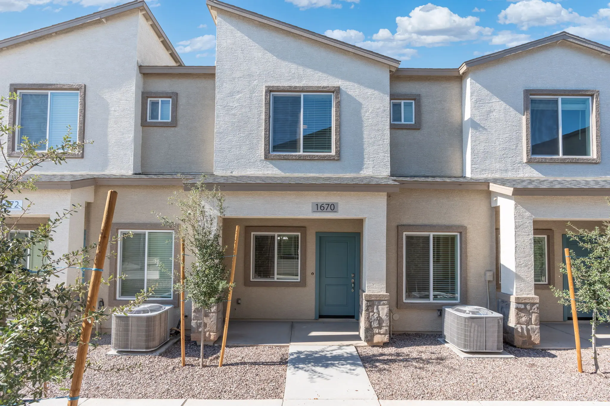 Front view of a modern townhouse with a blue door and landscaping, featuring air conditioning units outside.