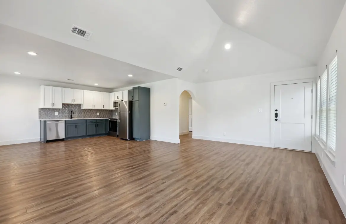 A spacious open concept living area with laminate flooring, modern kitchen in the back, and natural light from a front door with sidelights.