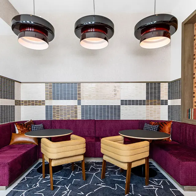 Stylish Cafe Interior A modern cafe interior featuring a purple upholstered booth with two yellow chairs and circular tables. The walls are decorated with various tiles, and there are pendant lights hanging from the ceiling.