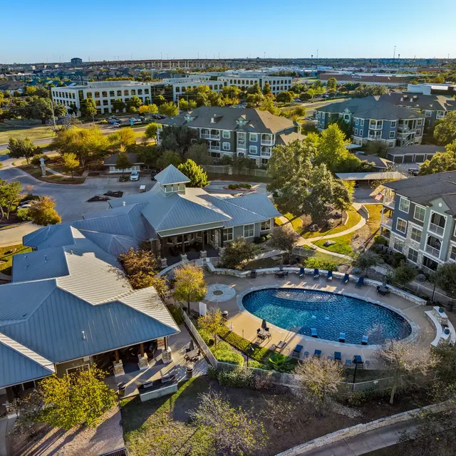 Aerial view of a modern apartment complex featuring a swimming pool surrounded by lush greenery and outdoor seating areas.